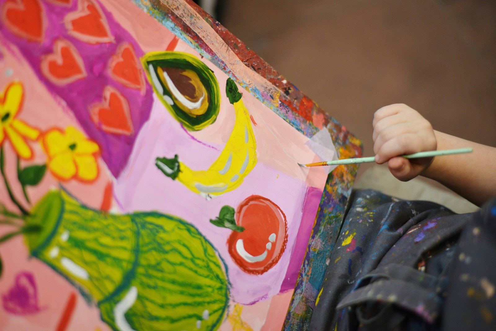 Child painting bright fruit shapes on a canvas